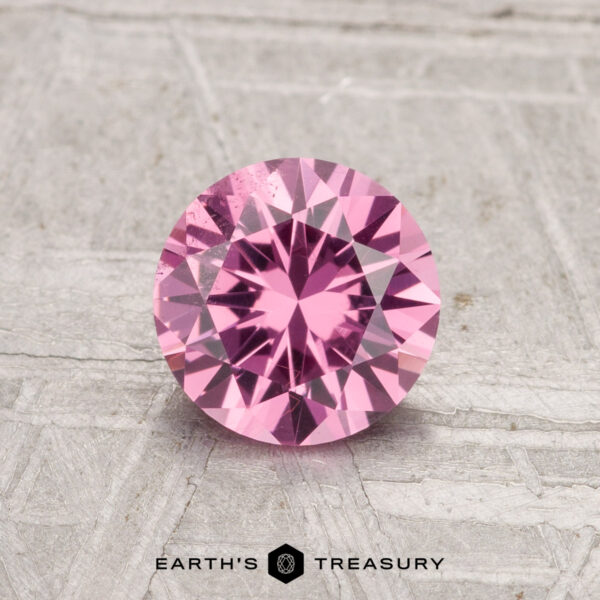 0.98-Carat Tanga Garnet A round, faceted 0.98-carat Tanga Garnet gemstone is displayed on a light gray textured background with the text "EARTH'S TREASURY" beneath it.