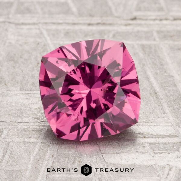 2.10-Carat Tanga Garnet The 2.10-Carat Tanga Garnet, cushion-cut and pink, is displayed on a textured gray surface with the "Earth's Treasury" logo at the bottom.