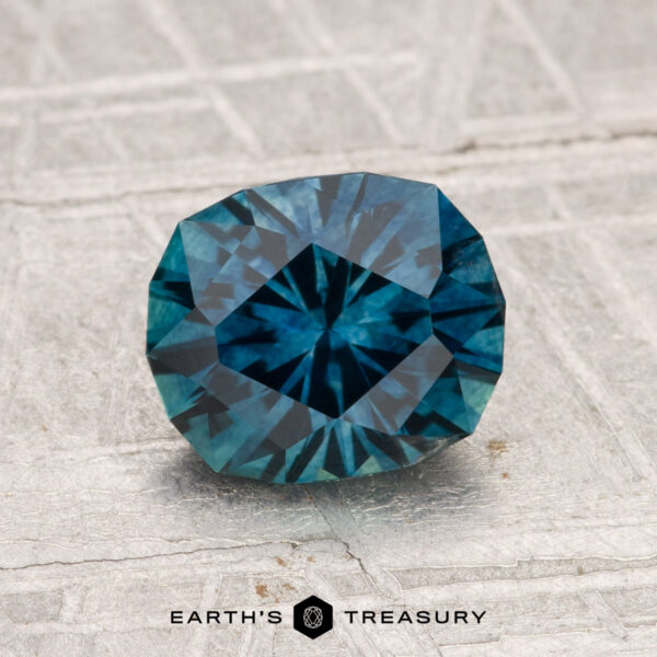 1.66-Carat Montana Sapphire (Heated) A 1.66-carat heated Montana sapphire, deep blue and faceted, is displayed on a textured light gray surface with "EARTH'S TREASURY" at the bottom.