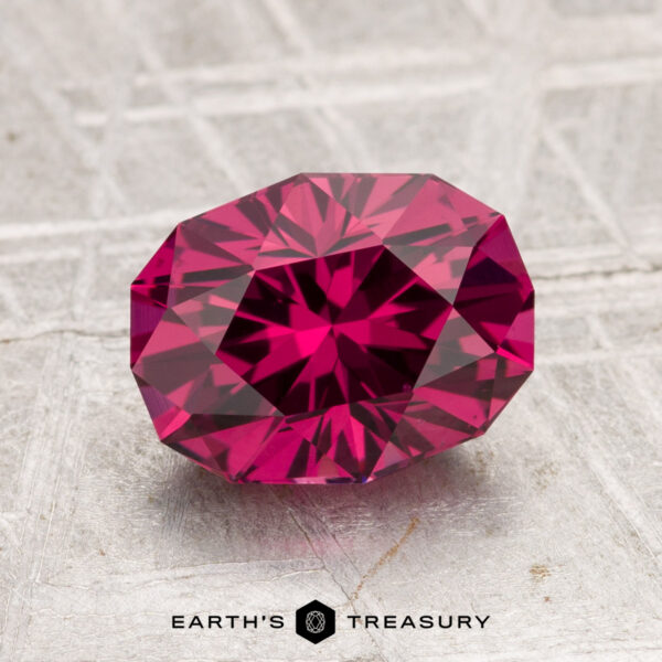 2.29-Carat Tanga Garnet A 2.29-carat Tanga Garnet, featuring a faceted deep pink hue, is displayed on a textured light-gray surface with "EARTH'S TREASURY" written below.