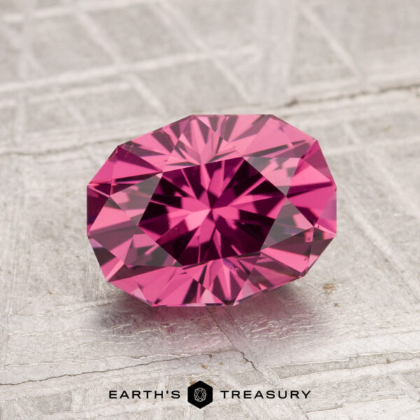 2.05-Carat Tanga Garnet A 2.05-carat Tanga Garnet, oval-cut and faceted, rests on a textured gray surface with "Earth's Treasury" displayed at the bottom.