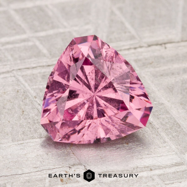 2.05-Carat Tanga Garnet A 2.05-carat Tanga Garnet, faceted in a triangular cut and pink in color, is displayed on a textured surface with the text "Earth's Treasury" at the bottom.
