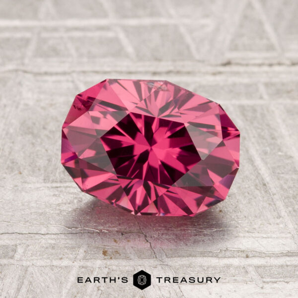 2.01-Carat Tanga Garnet A 2.01-carat Tanga Garnet, faceted in an oval shape, rests on a textured light gray surface with "EARTH'S TREASURY" at the bottom of the image.