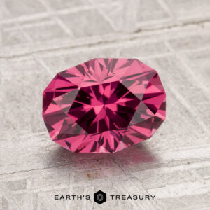 A 1.91-carat Tanga Garnet, cut in a faceted oval shape, is displayed on a textured gray surface with the Earth’s Treasury logo beneath it.