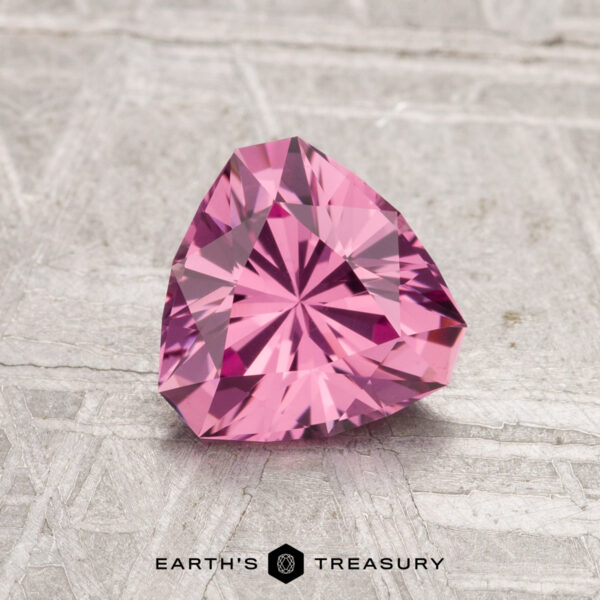 1.18-Carat Tanga Garnet A 1.18-carat faceted triangular Tanga Garnet is displayed on a textured light gray surface with the text "EARTH'S TREASURY" below.