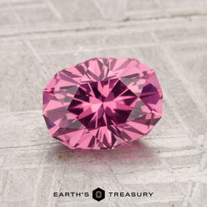 A 1.74-carat Tanga Garnet, faceted in an oval shape, displayed on a textured gray surface with "EARTH'S TREASURY" at the bottom.