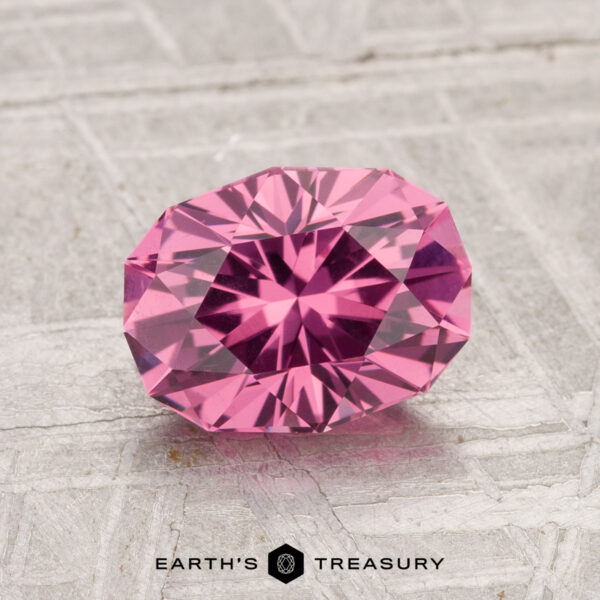 1.74-Carat Tanga Garnet A 1.74-carat Tanga Garnet, faceted in an oval shape, displayed on a textured gray surface with "EARTH'S TREASURY" at the bottom.