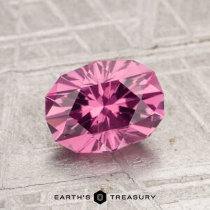 A 1.72-carat, faceted oval Tanga Garnet gemstone is shown on a textured metallic surface with "EARTH'S TREASURY" displayed at the bottom.