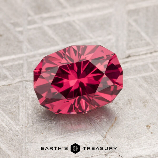 1.69-Carat Tanga Garnet A 1.69-carat Tanga Garnet, faceted in an oval shape, is displayed on a textured metallic surface with the text "EARTH'S TREASURY" at the bottom.