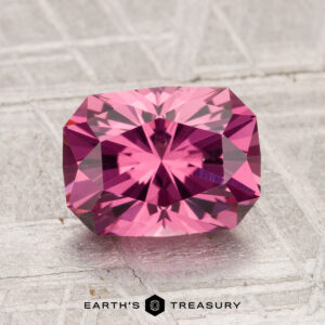 A 2.28-carat Tanga Garnet, rectangular step-cut with brilliant facets, is displayed on a textured grey surface. The "Earth's Treasury" logo and text appear at the bottom.