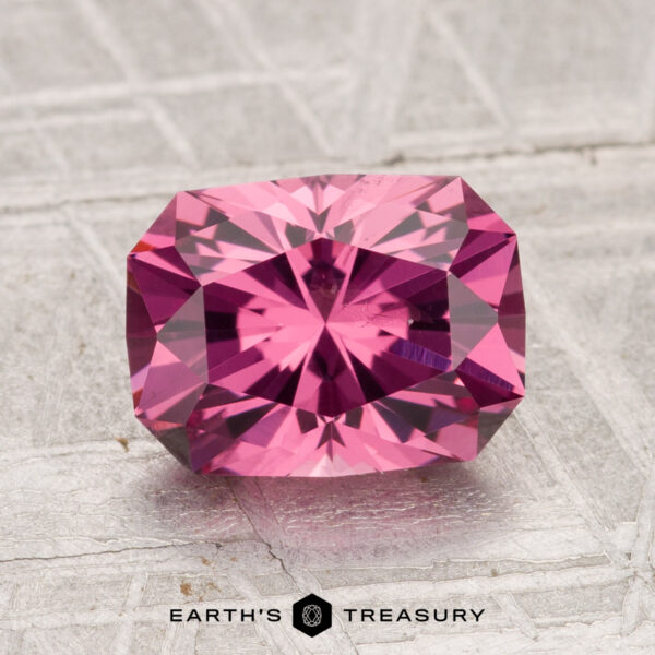 2.28-Carat Tanga Garnet A 2.28-carat Tanga Garnet, rectangular step-cut with brilliant facets, is displayed on a textured grey surface. The "Earth's Treasury" logo and text appear at the bottom.