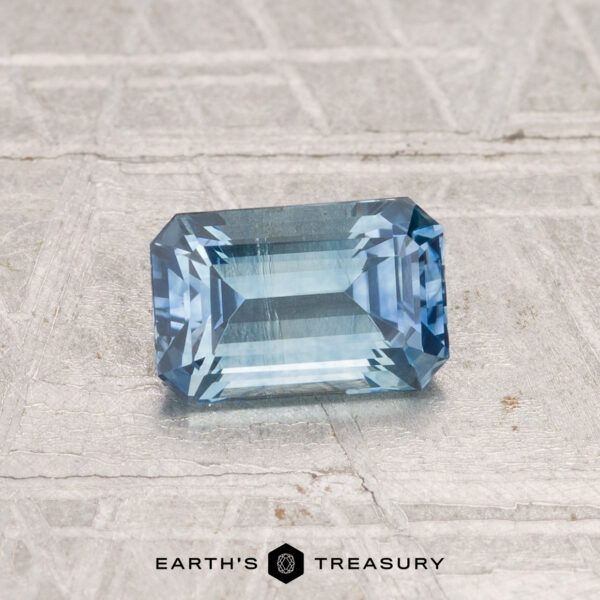 1.08-Carat Montana Sapphire (Heated) A rectangular, emerald-cut 1.08-carat heated Montana sapphire rests on a textured gray surface, with the Earth's Treasury logo below.