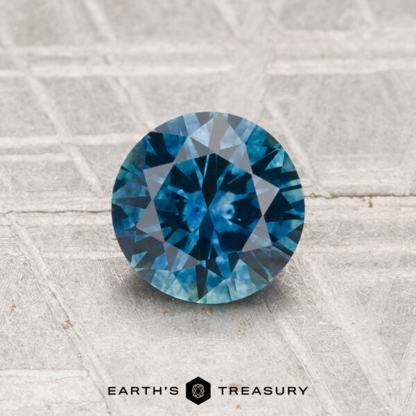 1.07-Carat Montana Sapphire (Heated) A 1.07-carat heated Montana sapphire with a round brilliant cut is displayed on a textured gray surface, with the text "EARTH'S TREASURY" below.