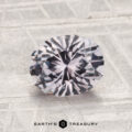 A 1.87-carat Montana sapphire with a round brilliant cut and faceted surface rests on a textured light gray background. The "Earth's Treasury" logo appears at the bottom of the image.