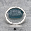 A textured blue rough gemstone is set in the "Amphitrite" band, crafted in 18K white gold with a notched edge, displayed on a mottled gray surface. "Earth's Treasury" is shown at the bottom.