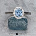 The "Alice" ring in platinum, featuring a 1.09-carat Montana sapphire surrounded by diamonds, is displayed atop a rough blue crystal with "Earth's Treasury" text below.