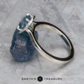The "Alice" ring in platinum with a 1.09-carat Montana sapphire is displayed against a rough blue stone on a textured gray surface. The Earth's Treasury logo appears at the bottom.