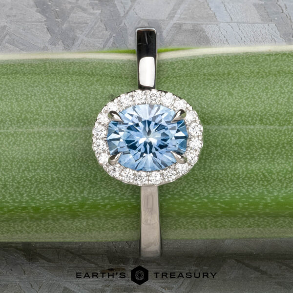 The "Alice" ring in platinum with 1.09-carat Montana sapphire The "Alice" ring in platinum, featuring a 1.09-carat Montana sapphire surrounded by a diamond halo, is displayed on a green surface.
