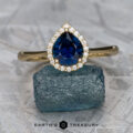 The "Margaret" ring in 14K yellow gold with a 1.06-carat Nigerian sapphire, surrounded by small diamonds, is displayed on a rough blue gemstone, with the text "EARTH'S TREASURY" below.