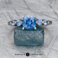 The "Lamia" ring in platinum featuring a 1.36-carat Montana sapphire stands upright on a rough blue stone, with the Earth's Treasury logo beneath.