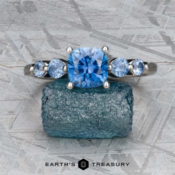The "Lamia" ring in platinum with 1.36-carat Montana sapphire The "Lamia" ring in platinum featuring a 1.36-carat Montana sapphire stands upright on a rough blue stone, with the Earth's Treasury logo beneath.