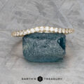 The Petite Pave Contour Band in 14K yellow gold is displayed on a rough blue gemstone against a textured gray background. The text "EARTH'S TREASURY" appears at the bottom.