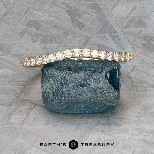 The Petite Pave Contour Band in 14K yellow gold The Petite Pave Contour Band in 14K yellow gold is displayed on a rough blue gemstone against a textured gray background. The text "EARTH'S TREASURY" appears at the bottom.
