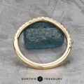 The Petite Pave Contour Band in 14K yellow gold is displayed upright, encircling a rough blue-green stone on a patterned metallic surface, with "EARTH'S TREASURY" shown at the bottom.