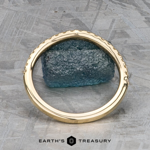 The Petite Pave Contour Band in 14K yellow gold The Petite Pave Contour Band in 14K yellow gold is displayed upright, encircling a rough blue-green stone on a patterned metallic surface, with "EARTH'S TREASURY" shown at the bottom.