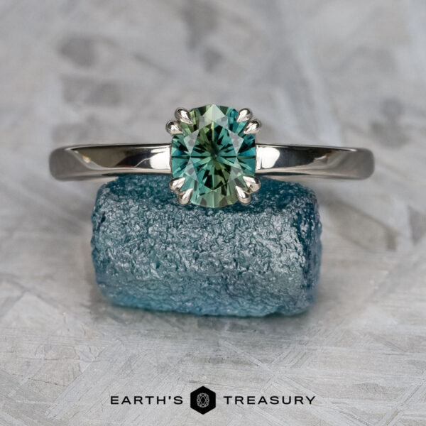 The “Capella” ring in platinum, smooth and polished, with 0.96-Carat Australian Sapphire The "Capella" ring in platinum, smooth and polished, features a 0.96-carat Australian sapphire. It stands upright on a textured blue-green crystal with the "Earth's Treasury" logo at the bottom.