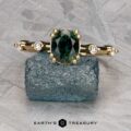 The "Pirouette" ring in 18K yellow gold features a 1.17-carat Australian Sapphire center and two clear side stones, displayed on a blue textured rock with the "Earth's Treasury" logo below.