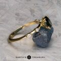 The "Pirouette" ring in 18K yellow gold with a 1.17-carat Australian Sapphire is shown resting on a rough blue stone, with the "Earth's Treasury" logo below.