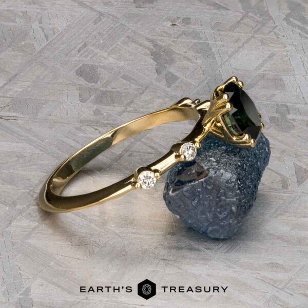 The "Pirouette" ring in 18K yellow gold with 1.17-carat Australian Sapphire The "Pirouette" ring in 18K yellow gold with a 1.17-carat Australian Sapphire is shown resting on a rough blue stone, with the "Earth's Treasury" logo below.