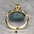 The "Pirouette" ring in 18K yellow gold with a 1.17-carat Australian Sapphire stands upright in prongs on a textured gray surface, with “EARTH'S TREASURY” displayed below.