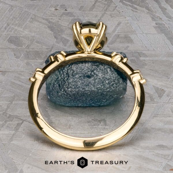 The "Pirouette" ring in 18K yellow gold with 1.17-carat Australian Sapphire The "Pirouette" ring in 18K yellow gold with a 1.17-carat Australian Sapphire stands upright in prongs on a textured gray surface, with “EARTH'S TREASURY” displayed below.