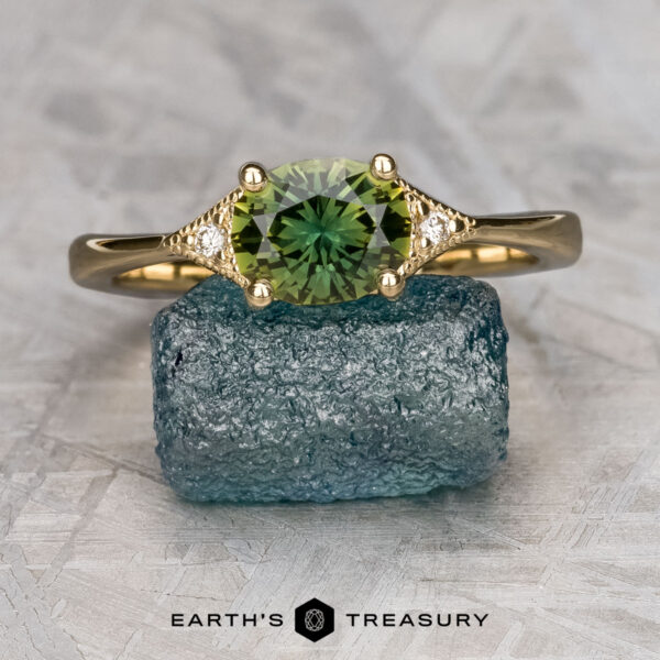 The "Niamh" ring in 14K yellow gold with 1.35-carat Australian sapphire The "Niamh" ring in 14K yellow gold, set with a 1.35-carat Australian sapphire and two small diamonds, is displayed on a rough blue stone above the text "EARTH'S TREASURY.