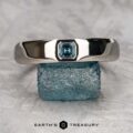 The "Shasta" ring in platinum with a teal sapphire, smooth and polished, is displayed balanced on a rough blue crystal, with the text "EARTH'S TREASURY" below.