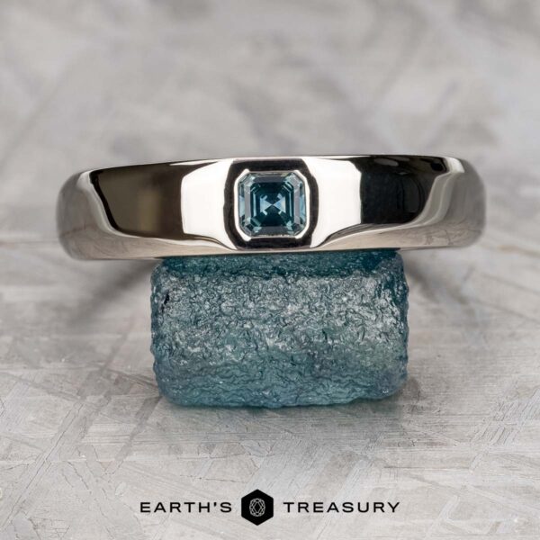The "Shasta" ring in platinum with teal sapphire, smooth and polished The "Shasta" ring in platinum with a teal sapphire, smooth and polished, is displayed balanced on a rough blue crystal, with the text "EARTH'S TREASURY" below.