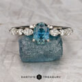The "Clemencia" ring in platinum with a 1.07-carat Montana sapphire rests on a rough blue crystal, with the "Earth's Treasury" logo below.