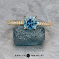 The Tapered Pave "Claire" ring in 18k yellow gold, featuring a 1.36-carat Montana sapphire and accent diamonds, is shown on a rough blue stone.
