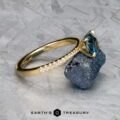 The Tapered Pave "Claire" ring in 18k yellow gold features a 1.36-carat Montana sapphire and pave diamonds on the band, displayed on a rough stone with the Earth's Treasury logo at the bottom.