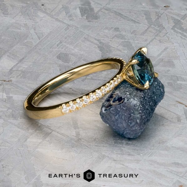 The Tapered Pave "Claire" ring in 18k yellow gold with 1.36-carat Montana sapphire The Tapered Pave "Claire" ring in 18k yellow gold features a 1.36-carat Montana sapphire and pave diamonds on the band, displayed on a rough stone with the Earth's Treasury logo at the bottom.