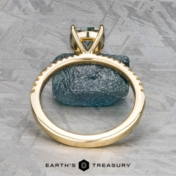 The Tapered Pave "Claire" ring in 18k yellow gold with 1.36-carat Montana sapphire The Tapered Pave "Claire" ring in 18k yellow gold with a 1.36-carat Montana sapphire stands upright on a blue-grey stone, viewed from the side. The "Earth's Treasury" logo appears at the bottom.