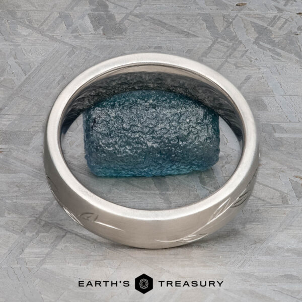 The "Olive" band in platinum The "Olive" band in platinum encircles a rough blue gemstone on a textured gray surface, with "EARTH'S TREASURY" displayed at the bottom.