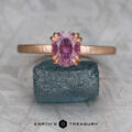 The “Capella” ring in 20K pink gold, hammered and brushed, with a 1.63-carat Umba Sapphire, stands upright on a rough blue-green stone. A light gray background and "EARTH'S TREASURY" text appear below.