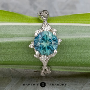 The "Juniper" ring in platinum features a 1.63-carat Montana sapphire in an ornate setting, displayed on a green leaf. The Earth's Treasury logo is shown at the bottom.