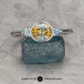 The "Evadne" ring in 14K white gold, featuring a 1.34-carat round Montana sapphire between two smaller blue gems, is shown on a rough blue mineral with the "Earth's Treasury" logo below.