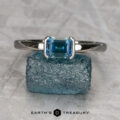 The "Larisa" ring in 14K white gold with a 0.92-carat Montana sapphire is displayed upright on a rough blue stone, with the Earth's Treasury logo below.