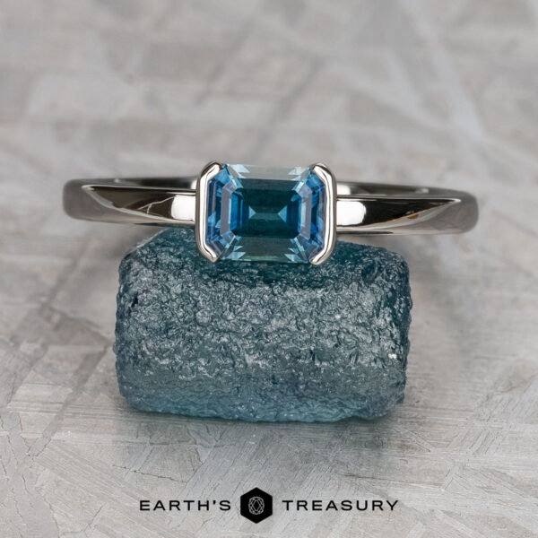 The "Larisa" ring in 14K white gold with 0.92-carat Montana sapphire The "Larisa" ring in 14K white gold with a 0.92-carat Montana sapphire is displayed upright on a rough blue stone, with the Earth's Treasury logo below.