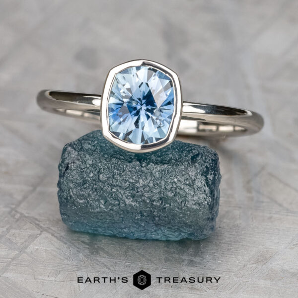 The "Deirdre" ring in platinum with 1.49-carat Montana sapphire The "Deirdre" ring in platinum, featuring a 1.49-carat faceted Montana sapphire, is displayed atop a rough blue crystal with the "Earth's Treasury" branding visible below.